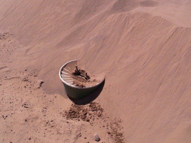 A Groasis Waterboxx almost covered entirely with sand in the Sahara Desert in Mexico